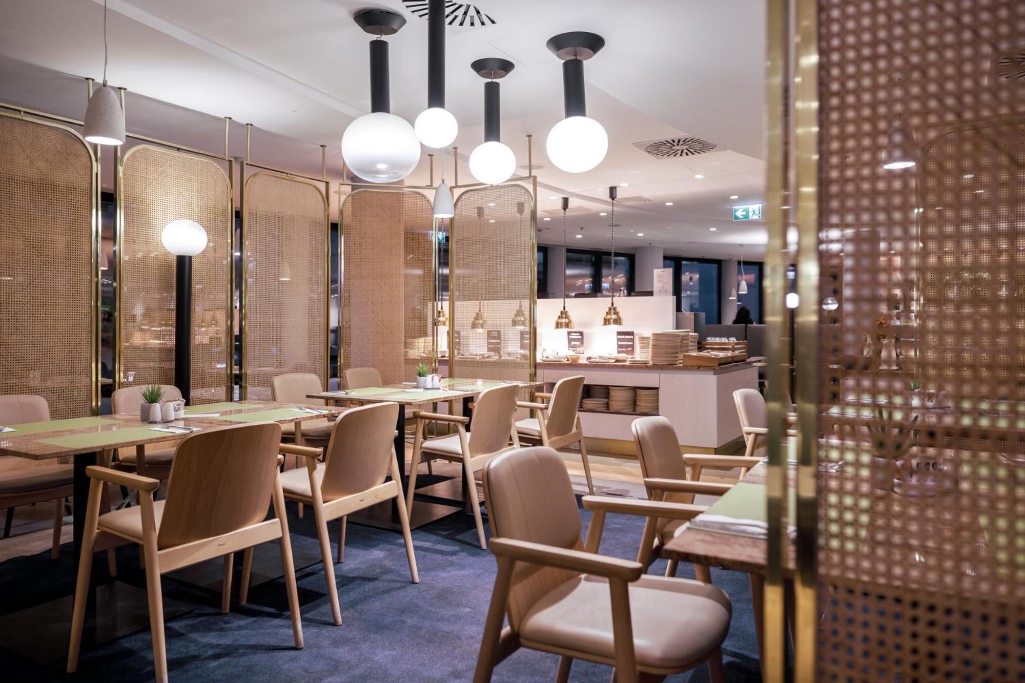 Radisson Blu Resort Swinoujscie Luaran gambar The photo shows a modern restaurant interior. There are wooden tables and chairs arranged neatly. The atmosphere appears warm and inviting, with soft lighting provided by round pendant lamps hanging from the ceiling. Partitions made of woven material