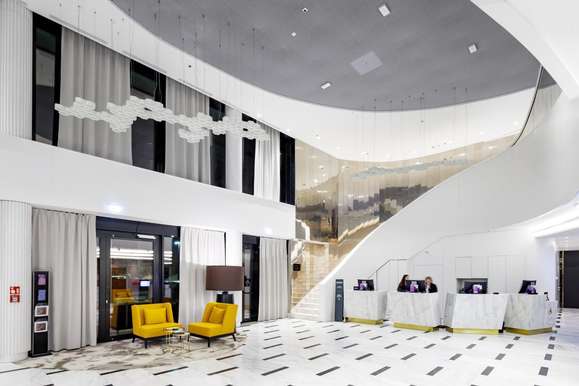 Radisson Blu Resort Swinoujscie Luaran gambar The photo shows a modern interior space, likely a hotel or a lobby area. It features a spacious, open design with high ceilings and a stylish staircase that leads to an upper level. The walls are mostly white, with large windows allowing natural ligh