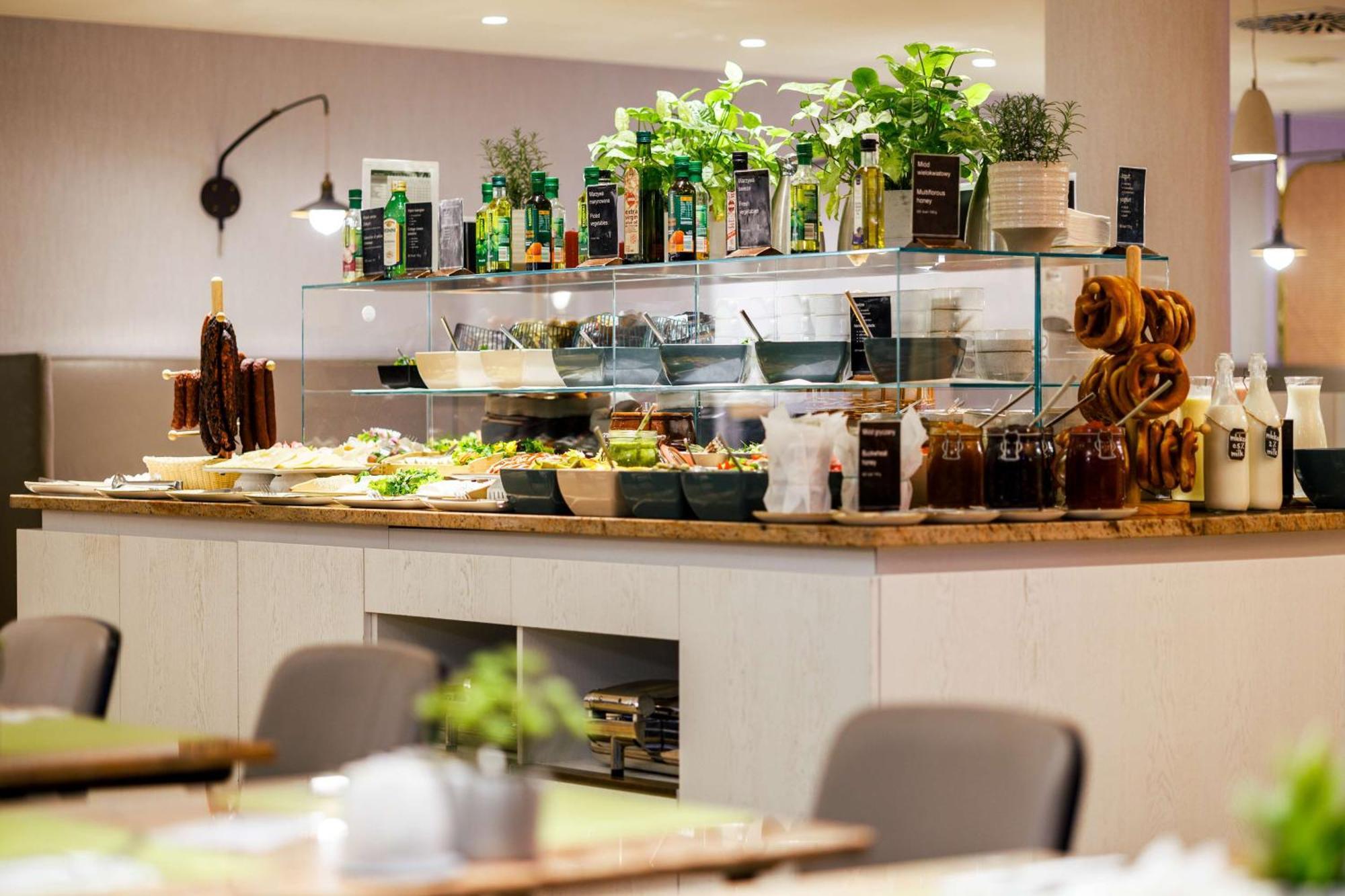 Radisson Blu Resort Swinoujscie Luaran gambar The photo shows a well-organized buffet display in a restaurant setting. There is a glass counter filled with various dishes. On the upper shelf, there are several bottles of oil and herbs, indicating a focus on fresh and healthy ingredients. Below t