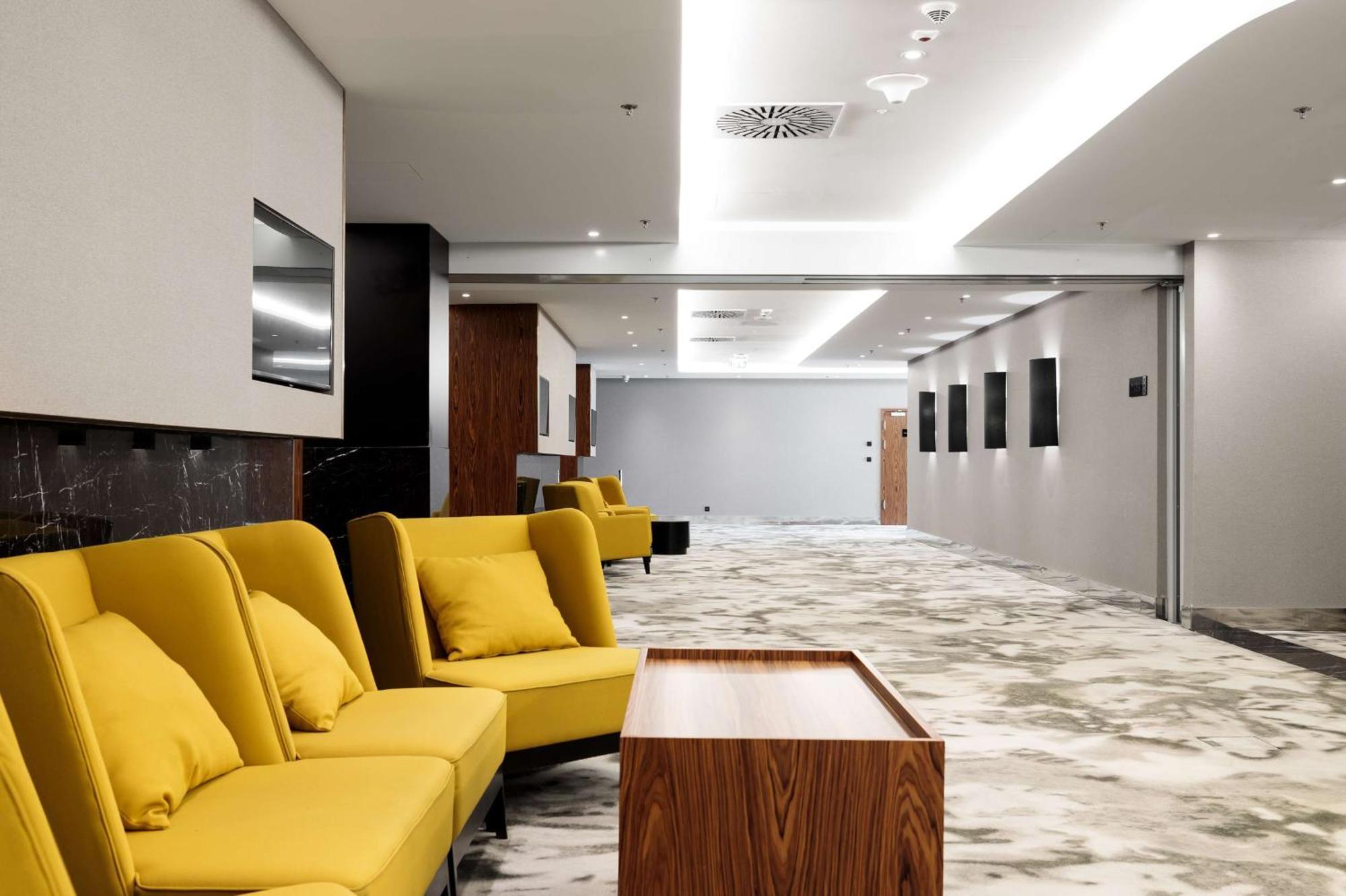 Radisson Blu Resort Swinoujscie Luaran gambar The photo shows a modern interior space, likely a lobby or waiting area. There are several yellow sofas with cushions arranged in a casual seating area. In front of the sofas, there is a wooden coffee table. The flooring features a gray and white mar