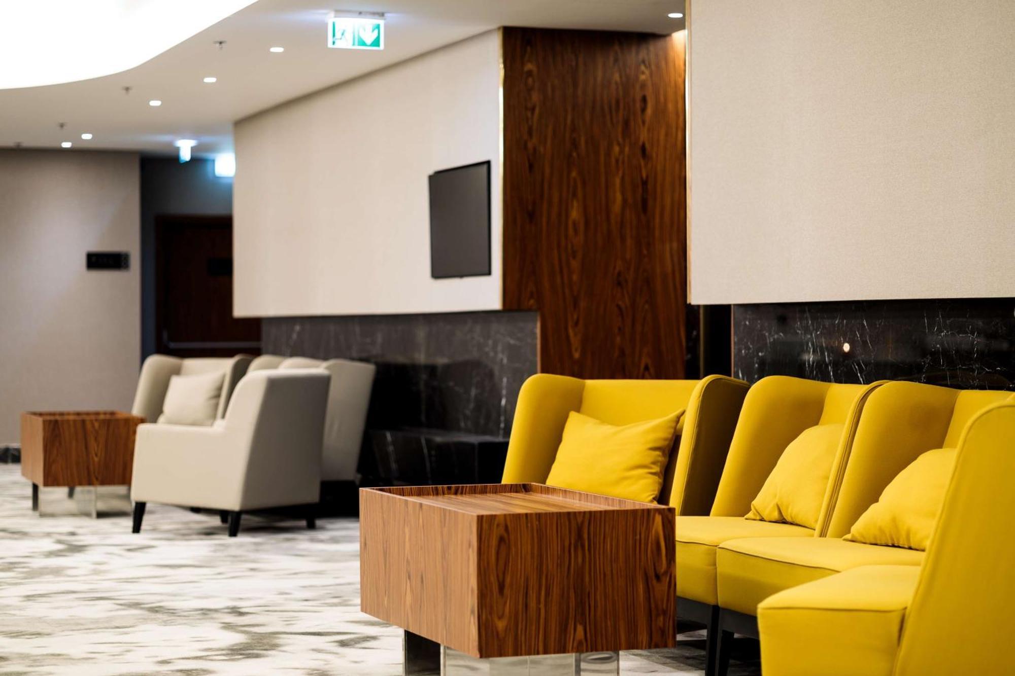 Radisson Blu Resort Swinoujscie Luaran gambar The photo depicts a modern lounge or waiting area with stylish seating. On the left, there are soft gray armchairs arranged around a wooden coffee table. In the center, there are yellow chairs with plush cushions, contributing a vibrant contrast to t