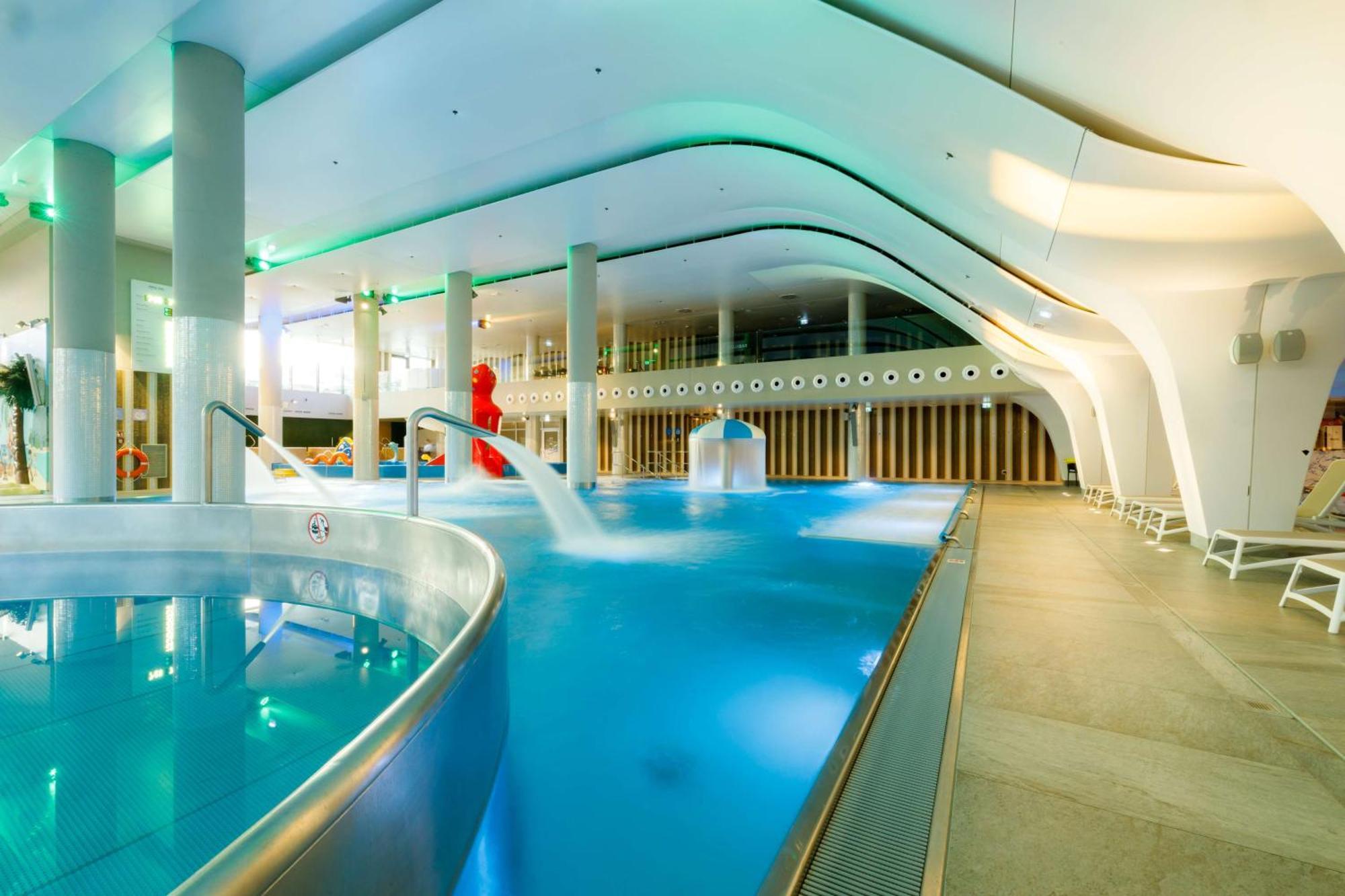 Radisson Blu Resort Swinoujscie Luaran gambar The photo shows a modern indoor swimming pool area with an elegant design. The pool features curved edges and is filled with clear, blue water. There are various amenities, such as jets for relaxation and possibly seating areas along the edges. The l