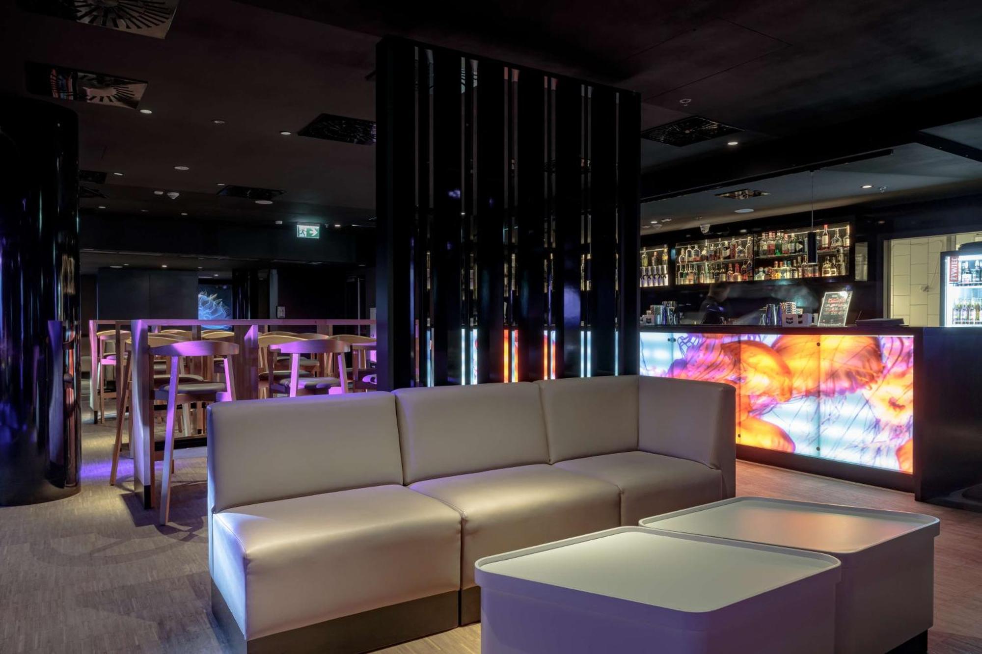 Radisson Blu Resort Swinoujscie Luaran gambar The photo depicts a modern interior space, possibly a lounge or bar. There are sleek, minimalistic furniture pieces, including a large, curved sofa and contemporary coffee tables. The lighting is dim, with a blend of colorful ambient lights illuminat