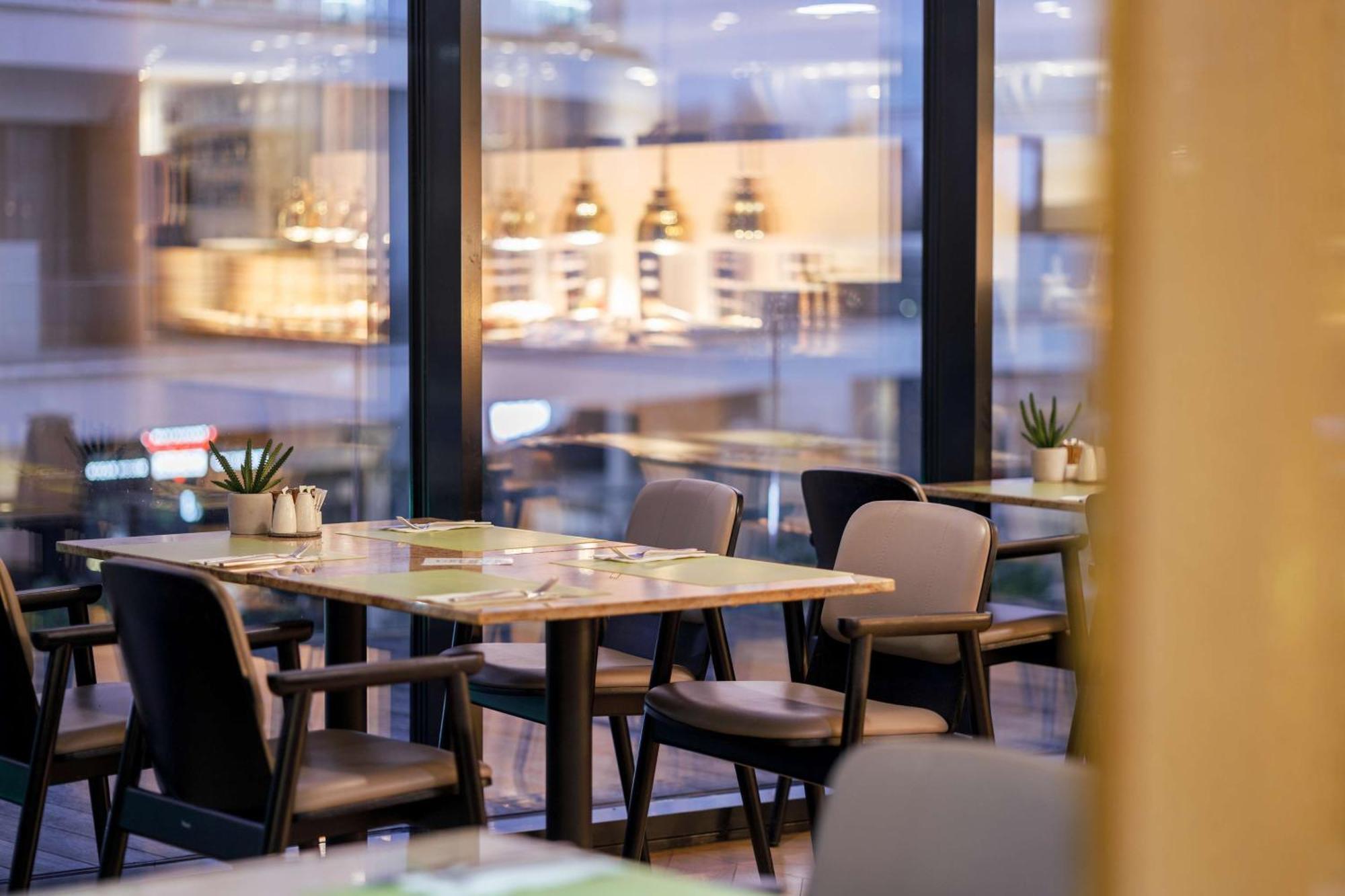 Radisson Blu Resort Swinoujscie Luaran gambar The photo shows a modern restaurant interior featuring several tables and chairs arranged under large windows. The tables are set with green placemats and cutlery. There are small potted plants on the tables, adding a touch of decor. In the backgroun