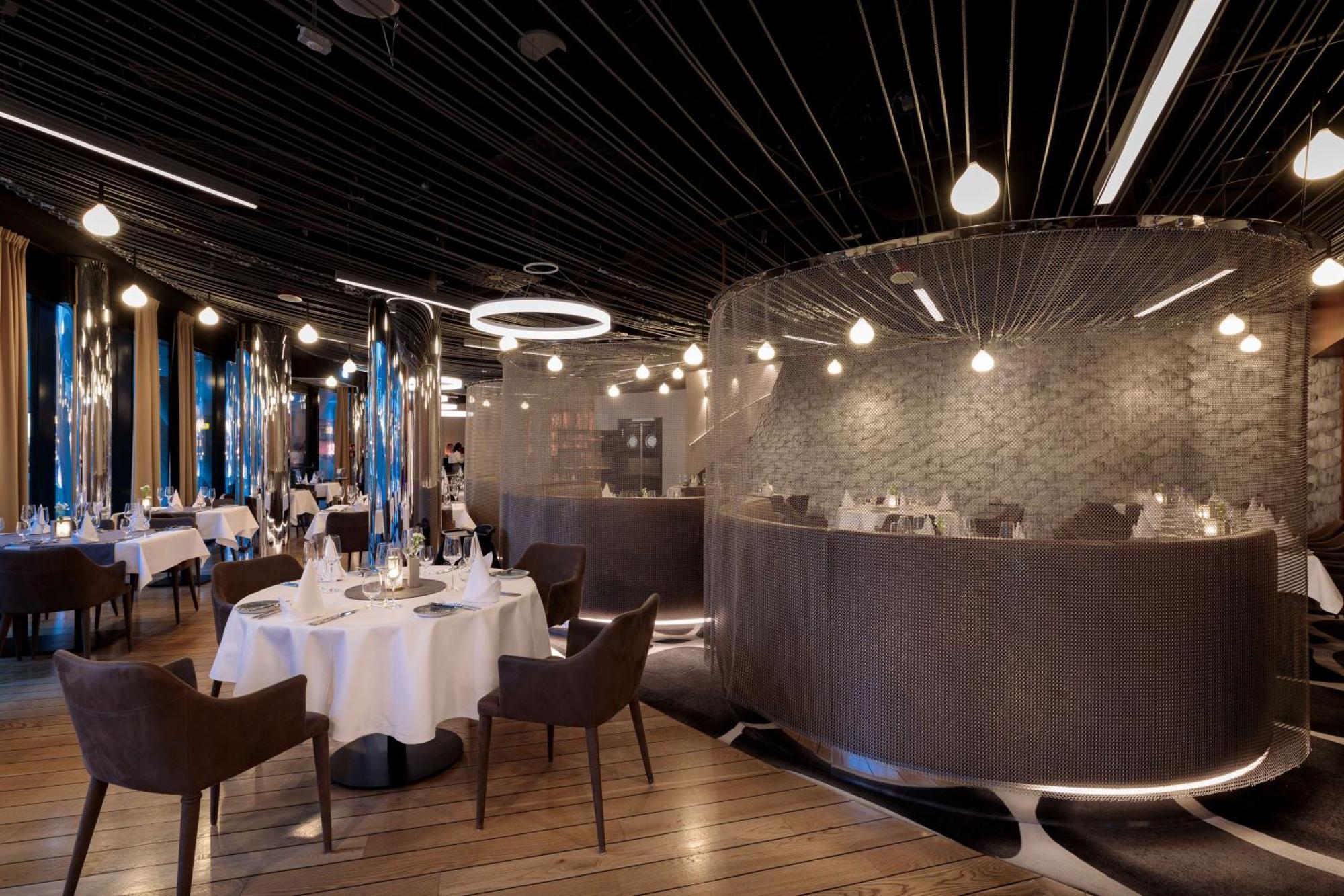 Radisson Blu Resort Swinoujscie Luaran gambar The photo shows an elegant restaurant interior. It features polished wooden floors and contemporary decor. Round tables are set with white tablecloths and have chairs arranged around them. The lighting is modern, with multiple pendant lights hanging 