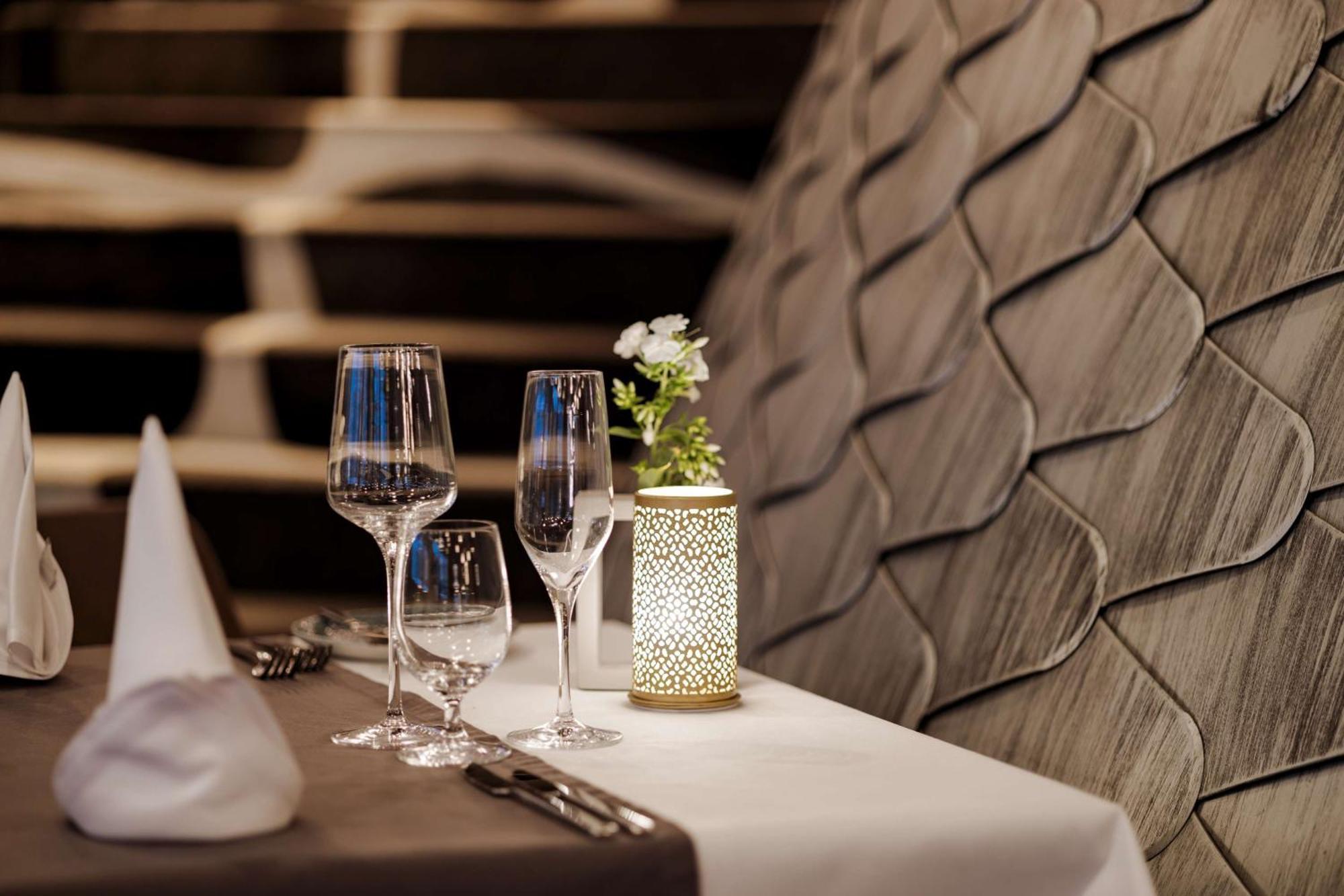 Radisson Blu Resort Swinoujscie Luaran gambar The photo shows a beautifully arranged table setting in a restaurant. There are two elegant wine glasses and a smaller glass, likely for water, placed on a crisp white tablecloth. A decorative lantern with intricate designs holds a small flower arran