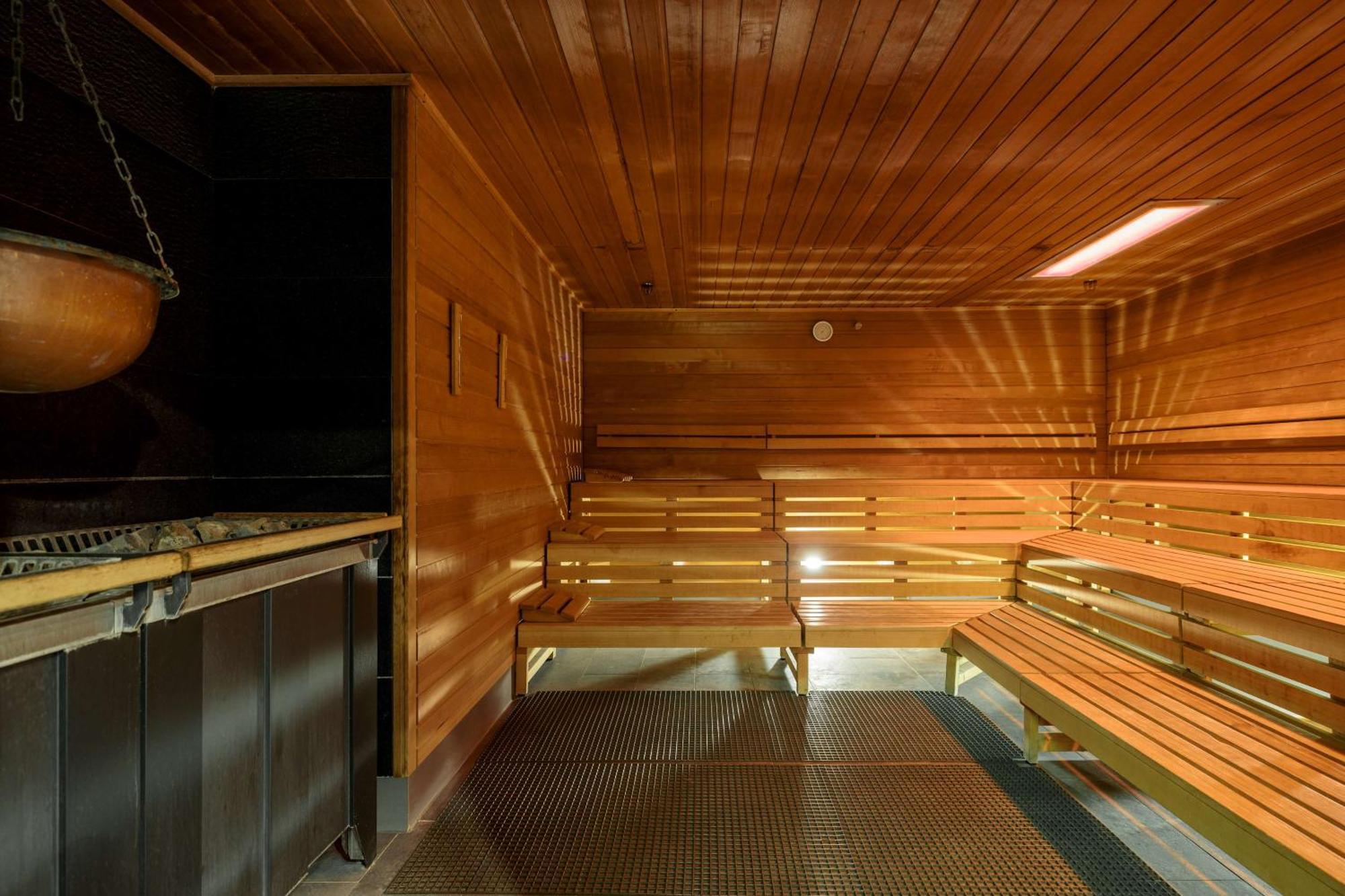 Radisson Blu Resort Swinoujscie Luaran gambar The photo shows the interior of a sauna. The walls and benches are made of wood, creating a warm and inviting atmosphere. There is a heater, likely for generating steam, and a metal rack connected to it, perhaps for holding stones or water. The desig