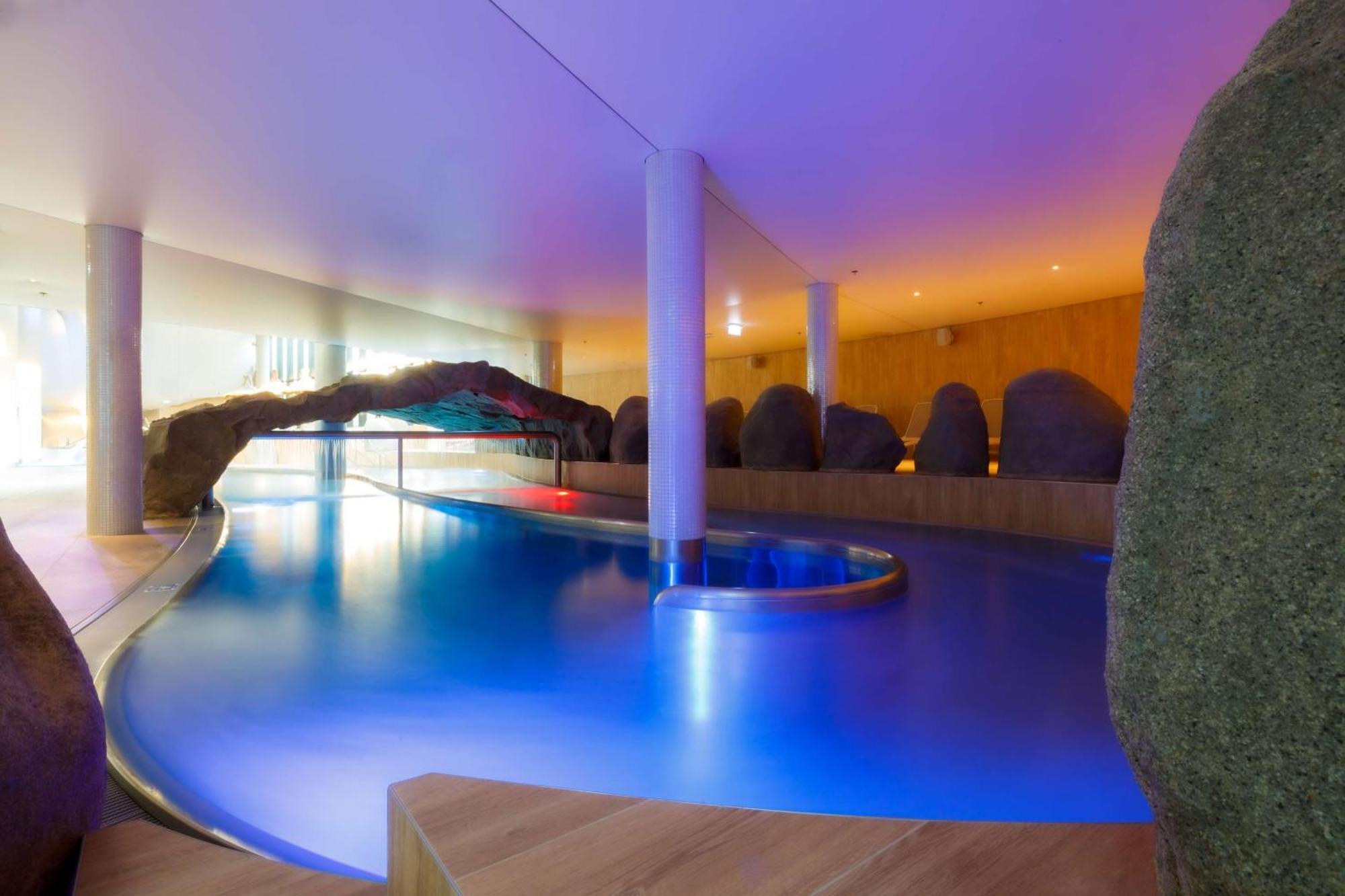 Radisson Blu Resort Swinoujscie Luaran gambar The photo showcases an elegant indoor swimming pool area. The pool has a flowing, organic shape and is illuminated with soft blue and purple lighting, creating a calming ambiance. Surrounding the pool are smooth, natural-looking stones and wooden ele