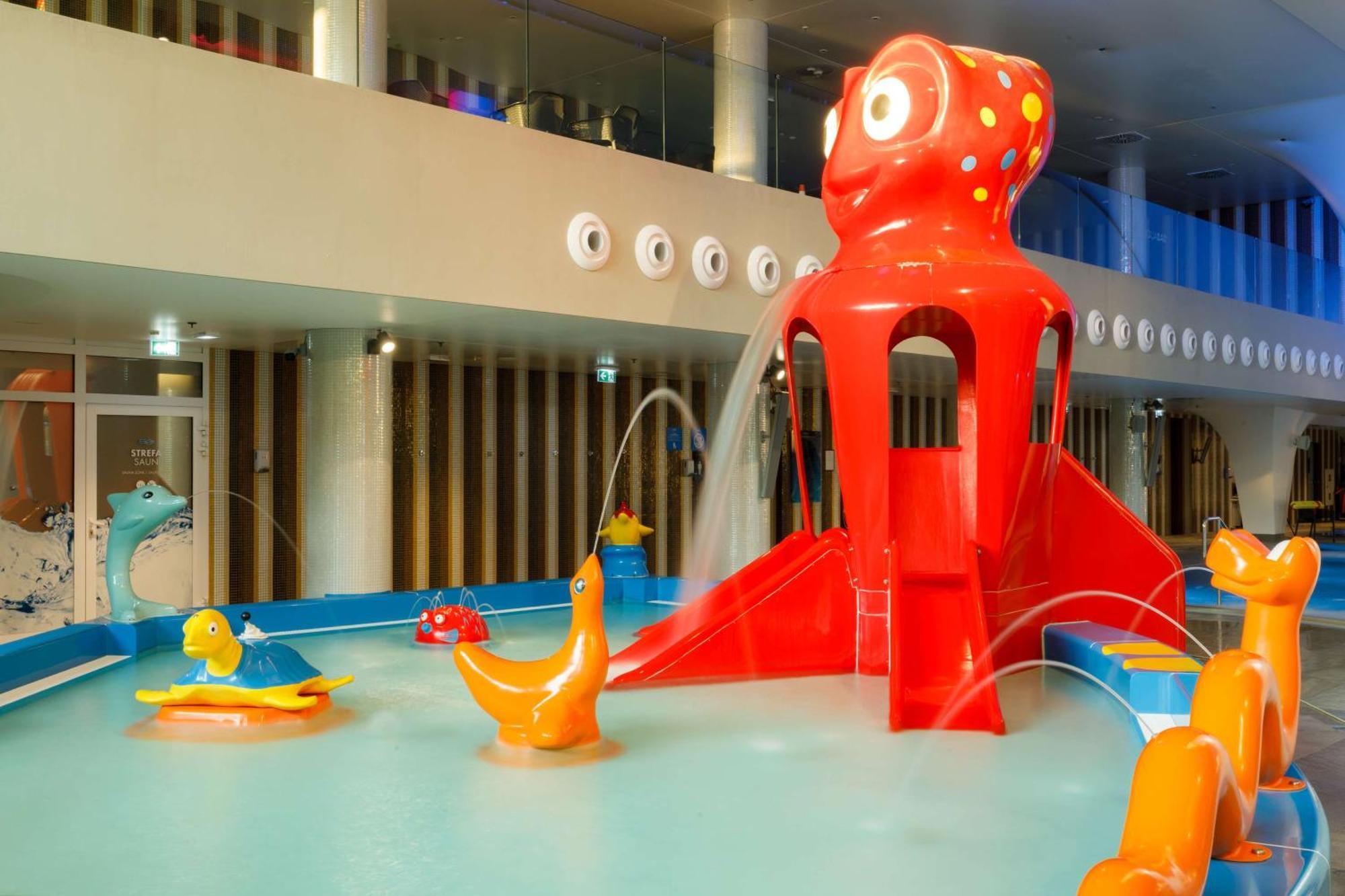 Radisson Blu Resort Swinoujscie Luaran gambar The photo shows a colorful indoor splash pad or water play area designed for children. Central to the scene is a large, bright red octopus structure, which has water fountains spraying out. Surrounding it are various playful, colorful water animals, 